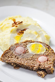 meat loaf filled with egg and sausage served with mashed potatoes and fried onion