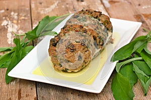 Meat loaf with fresh green buckrams leaves on white plate on wooden background