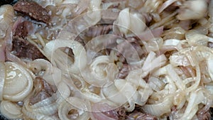 Meat with lots of onions is fried in boiling oil. Cooking pilaf or goulash. Close-up of hot food. Stirring the products