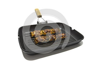 Meat and pepper skewers in a non-stick frying pan, isolated on white background.