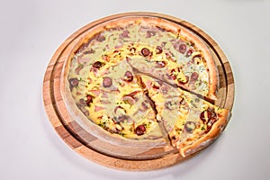 Meat pizza with hunting sausages on round wooden cutting board isolated on background