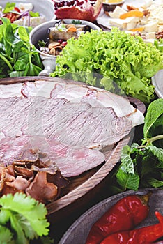 Meat platter with selection of different kinds of meat served on a wooden board with a lot of fresh greenery around.