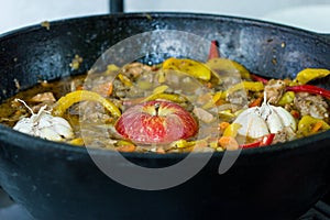 Meat with potatoes, apples and garlic in a cauldron on fire
