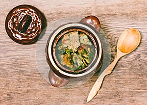 Meat with potatoes in a clay pot and a wooden spoon on table