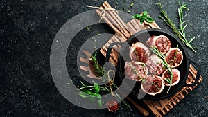 Meat. Raw Meat Veal medallions wrapped in bacon. Laid out in a pan, ready to cook. On a black concrete background.