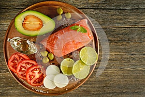 Meat red salmon fish, tomatoes, spices, lemon, green olives on wooden kitchen table.