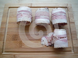 meat rolls in bacon on a wooden table, the cooking process