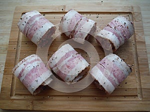meat rolls in bacon on a wooden table, the cooking process