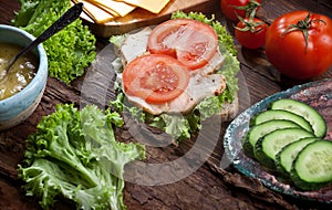 Meat sandwich with fresh tomatoes, green salad, cucumbers, cheese and sauce on dark wooden table background