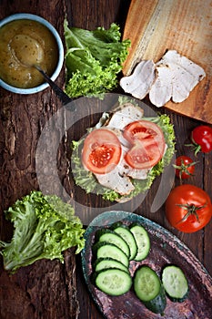 Meat sandwich, green salad and vegetables on dark wooden table background