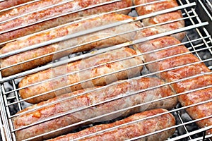 Meat sausages squeezed between grill grates, frying on a grill brazier.