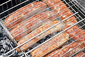 Meat sausages squeezed between grill grates, frying on a grill brazier.