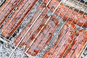 Meat sausages squeezed between grill grates, frying on a grill brazier. Closeup