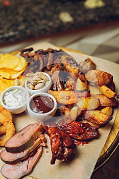 Meat set on a wooden board. Fried chicken wings, pork ribs, grilled vegetables, french fries. Beer appetizer with sauces