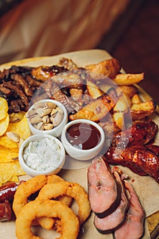 Meat set on a wooden board. Fried chicken wings, pork ribs, grilled vegetables, french fries. Beer appetizer with sauces