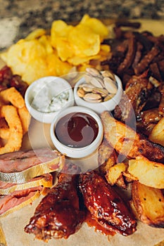 Meat set on a wooden board. Fried chicken wings, pork ribs, grilled vegetables, french fries. Beer appetizer with sauces