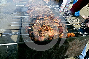 Meat on skewers fried on the grill in the open air, visible hands of the cook