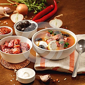 Meat Solyanka soup on with ingridients, sausage, olive,lemon, parsley, garlic, yogurt. Ukrainian food. Wooden background