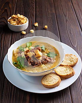 Meat soup with croutons in a white plate on a wooden table