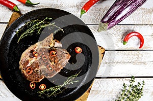 Meat with spices in a pan, rosemary, and hot chili peppers on a white wooden table background