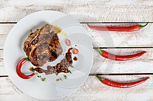 Meat with spices in a pan, rosemary, and hot chili peppers on a white wooden table background