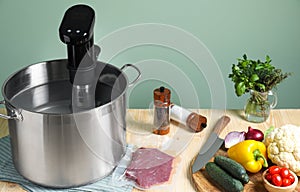 Meat in vacuum packing and other ingredients near pot with sous vide cooker on wooden table. Thermal immersion circulator