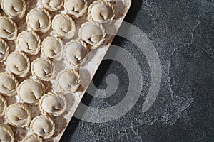 Meat or vegeterian dumplings, pelmeni on a wooden board on a dark grey table. Russian national food. Close up top view.