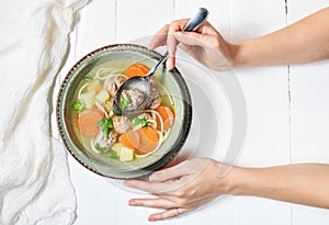 Meatball soup and ingredients on white wooden table. Female hands holds spoon.