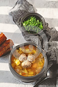 Meatball in a spoon. soup with meatballs in a black bowl and croutons in hard light. A European dish typical of Spain