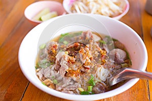 Meatballs and meat with wide rice noodles in soup was added pickled chili on top in a white bowl  on woody background. It is a