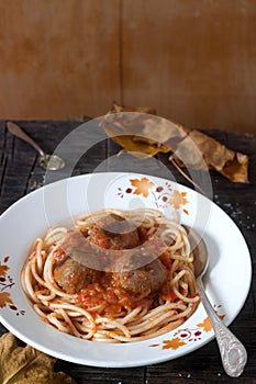 Meatballs in a sauce with pasta on a wooden background with autumn leaves. Rustic style.