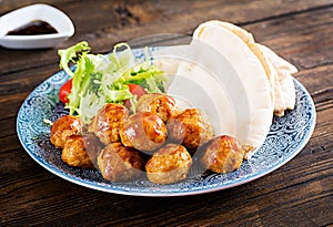 Meatballs in sweet and sour glaze on a plate with pita bread and vegetables