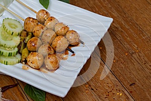 Meatballs toasted on wood dish and a sauce decorated with coriander placed on the table brown wood. Grill pork balls pour at