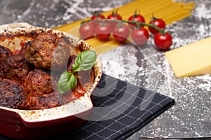 Meatballs with tomato sauce and decorated with basil leaf, served in white and red pan on grey background. next to the pan near
