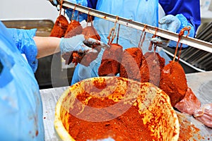 Meatpacking staff seasoning pieces of fresh pork and hanging on hooks on a metal rack for smoking and marinating