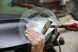 mechanic is aligning car body part by hammer