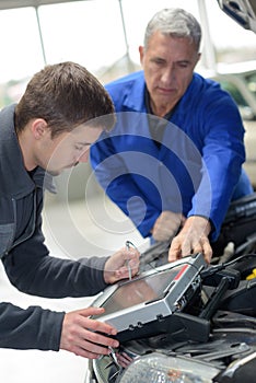 Mechanic and apprentice working on car with computer