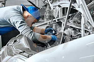 Mechanic in blue overalls checking serviceability of car engine