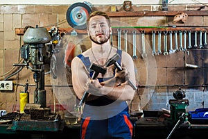 Mechanic in a car garage stands at the desktop with hammers in his hands.