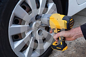 Mechanic changing a car tire in a workshop using an electric drill to loosen the bolts in a concept of service or replacement car