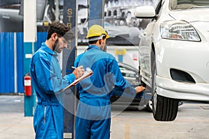 Mechanic checks the car fixing list while his assistant lifting the white car for examining the bottom. Auto car repair service.