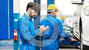 Mechanic checks the car fixing list while his assistant lifting the white car for examining the bottom. Auto car repair service