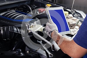 The mechanic checks the engine using tablet computer technology. Complete with wrench tool Auto mechanic working in the garage.