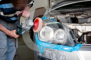 Mechanic cleaning headlights and polishing with power buffer photo