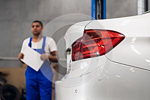 A mechanic with a clipboard inspects car. Background