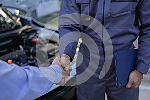 Mechanic with clipboard and man or owner shaking hands at car shop, male customer and technician