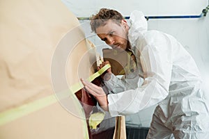 Mechanic covering car body with paper and masking tape before painting in auto repair service.