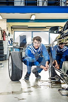 Mechanic Crouching While Changing Car Tire At Garage