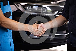 Mechanic and customer shaking hands in an auto repair shop, car service. Two unrecognizable men auto mechanic and client