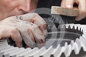 Mechanic with dirty hands cleaning a cog wheel with a steel brush